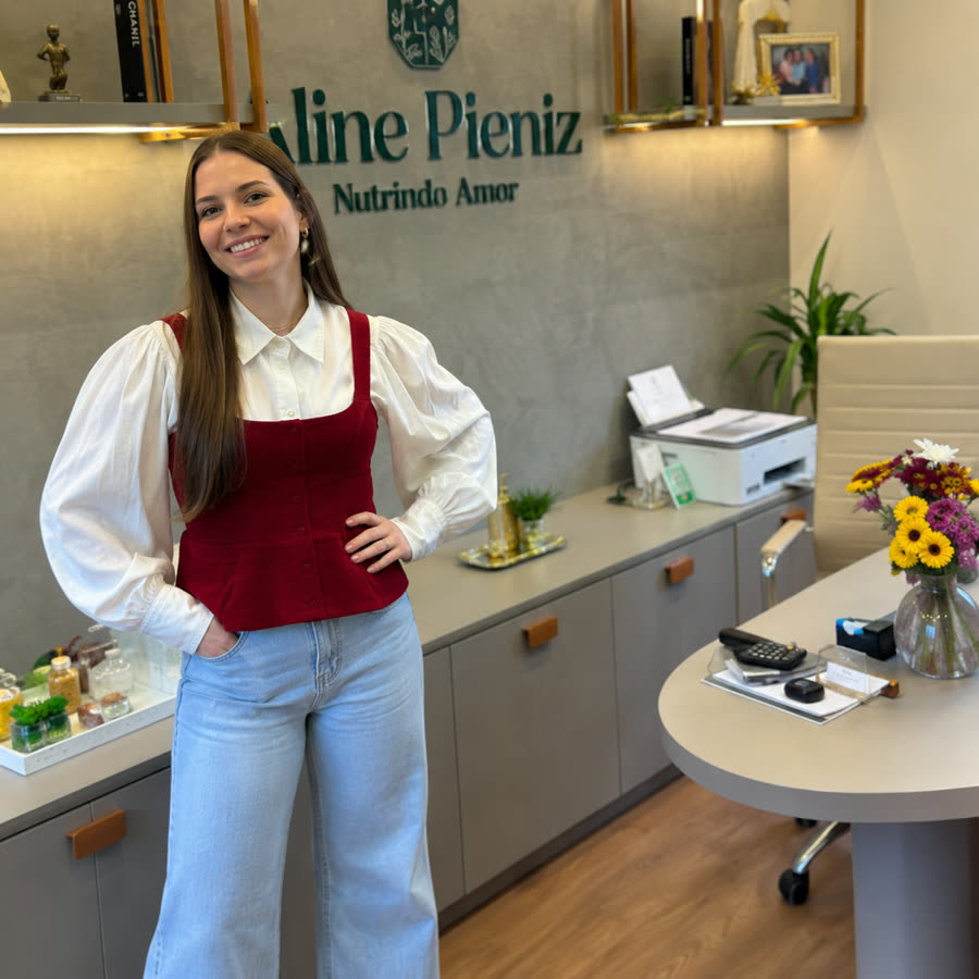 Aline Pieniz em pé no consultório, ao lado da sua marca